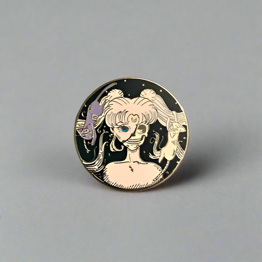 Circular pin with a design of a woman with black hair and white face on a gray surface.