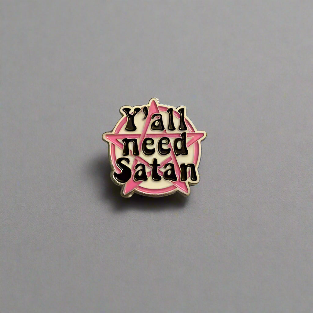 Pin with 'Y'all need Satan' text on a gray surface