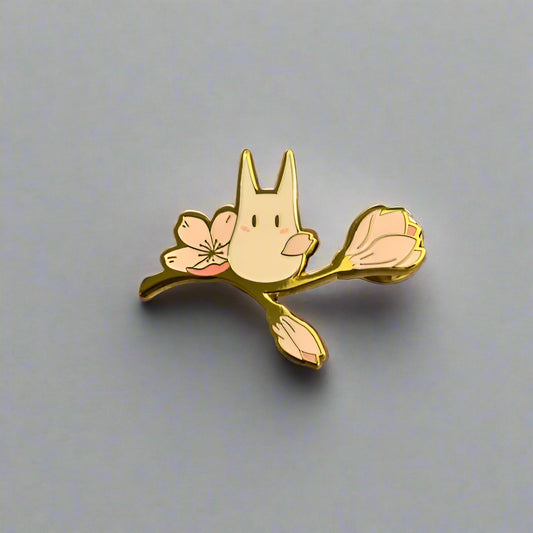 Enamel pin of a cartoon-like creature with floral wings on a gray background
