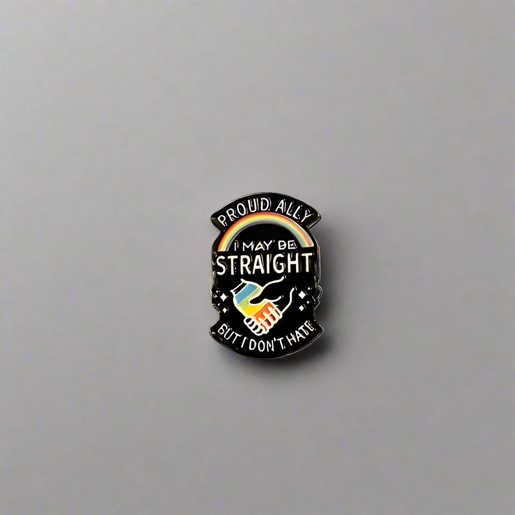 Pin with rainbow design and text on a gray surface