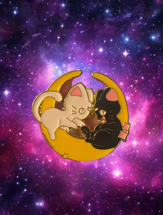 A pin featuring a whimsical design with two cats and a crescent moon.