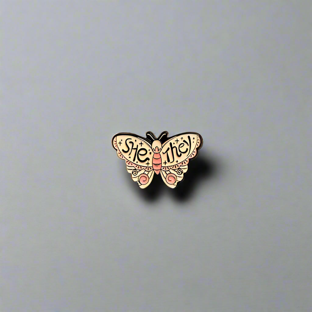 Butterfly-shaped pin with text on a gray surface