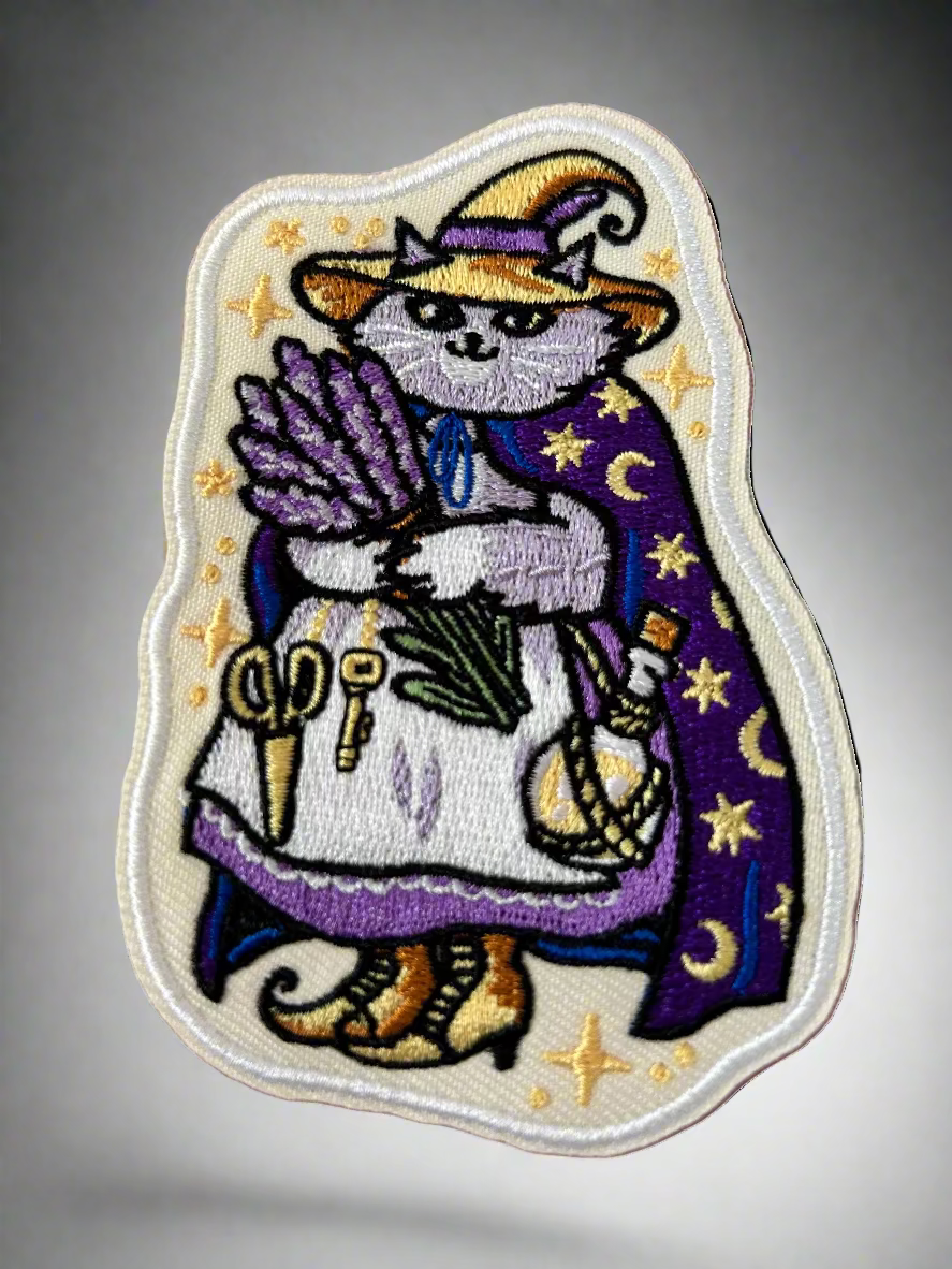 Embroidered patch of a cat in a witch costume with stars and moons on a pink background