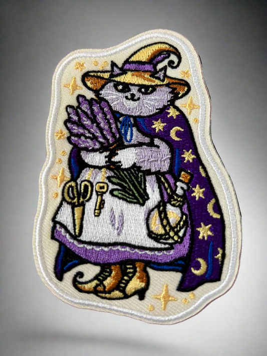 Embroidered patch of a cat in a witch costume with stars and moons on a pink background